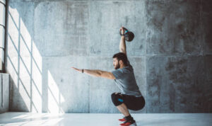Male fitness athlete performing overhead squat with kettlebell